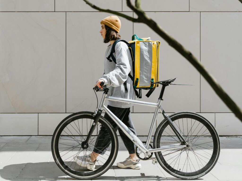 A woman walking beside a bicycle with a thermal backpack, representing urban food delivery.